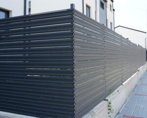 Un gard metalic orizontal modern, gri închis, mărginește un trotuar lângă o clădire bej, transmițând siguranță și design contemporan.