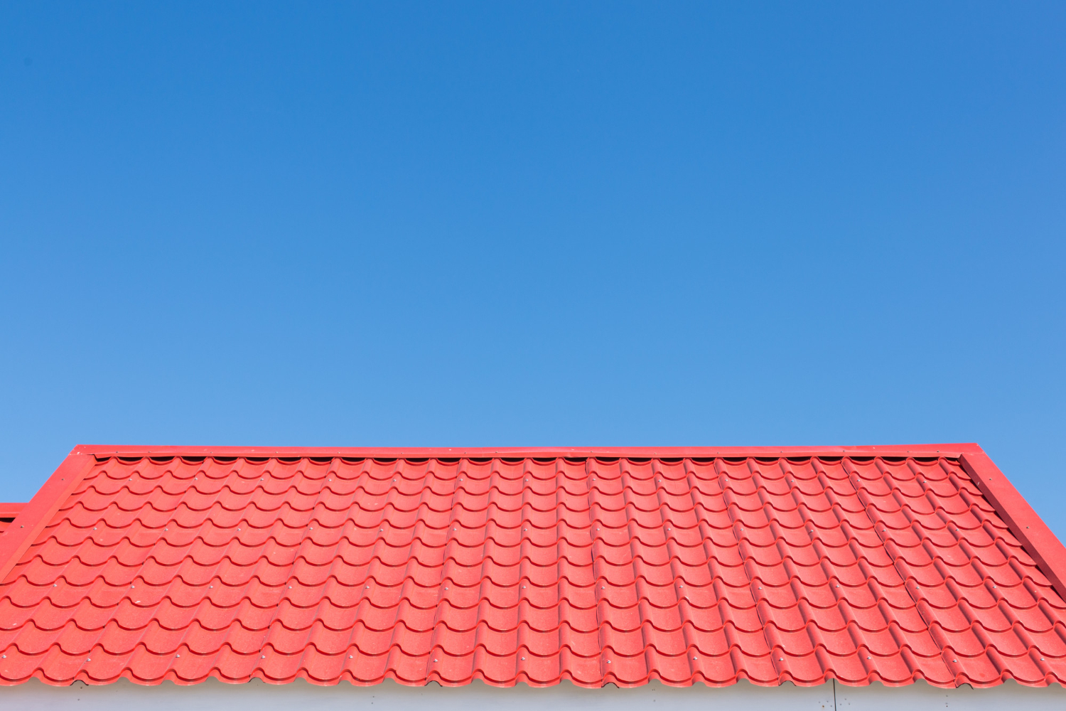 Un acoperiș cu țigle roșii aprinse pe un cer albastru senin. Culorile strălucitoare și liniile simple transmit o estetică curată, veselă și minimalistă.