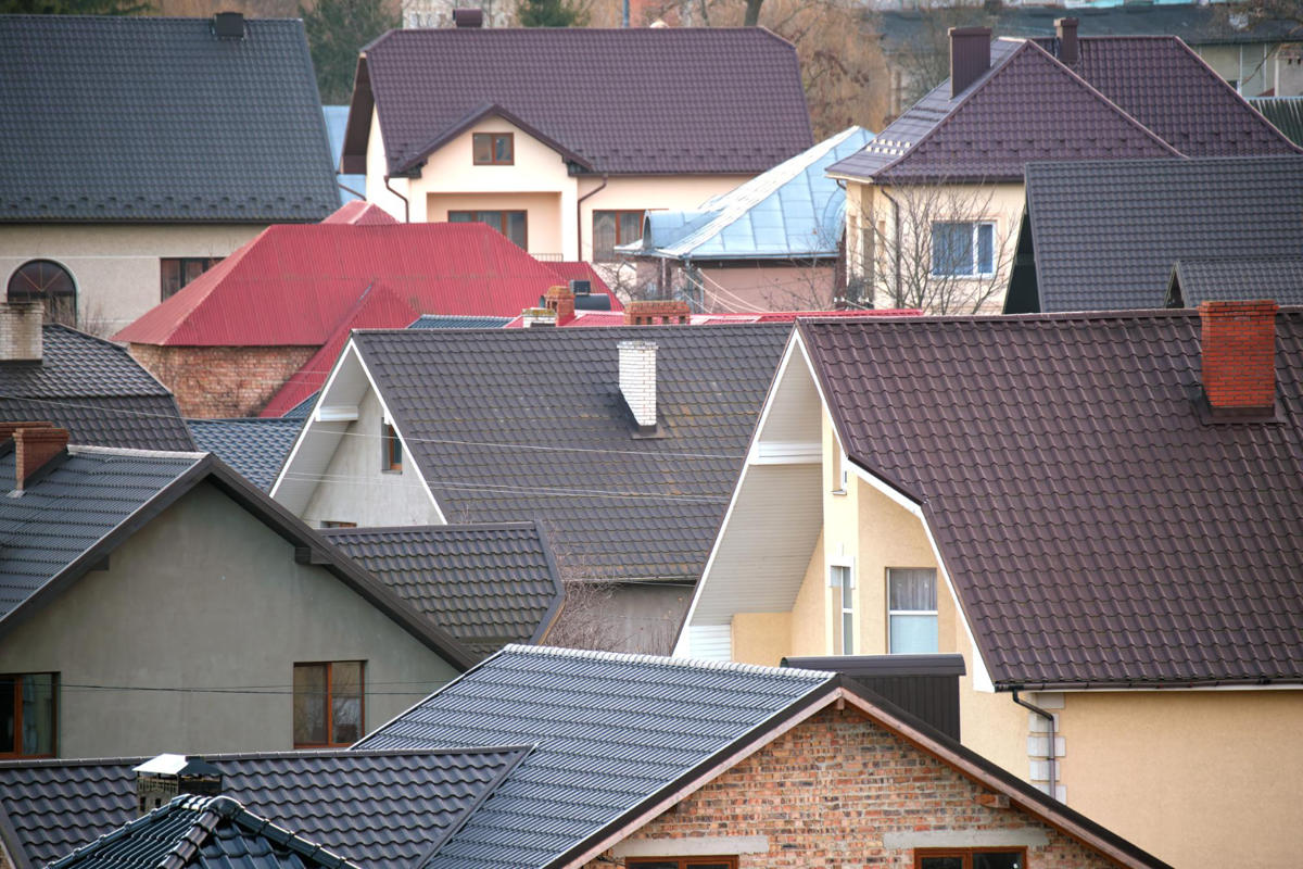 Un ansamblu de case din suburbii, cu acoperișuri de diferite stiluri și culori, printre care roșu, maro și gri. Imaginea redă atmosfera unui cartier confortabil și liniștit.